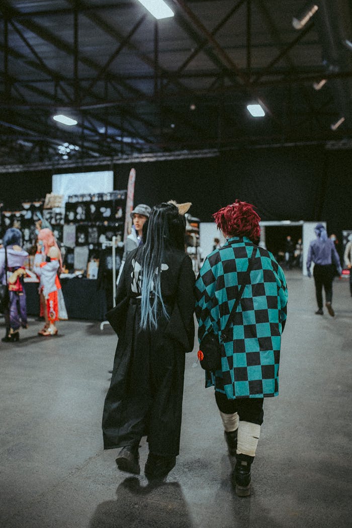 Two people dressed in cosplay costumes walking through an indoor convention hall.